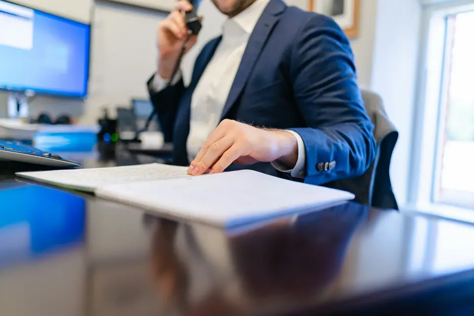 Au bureau, un homme déjà au téléphone pose la main sur un dossier.